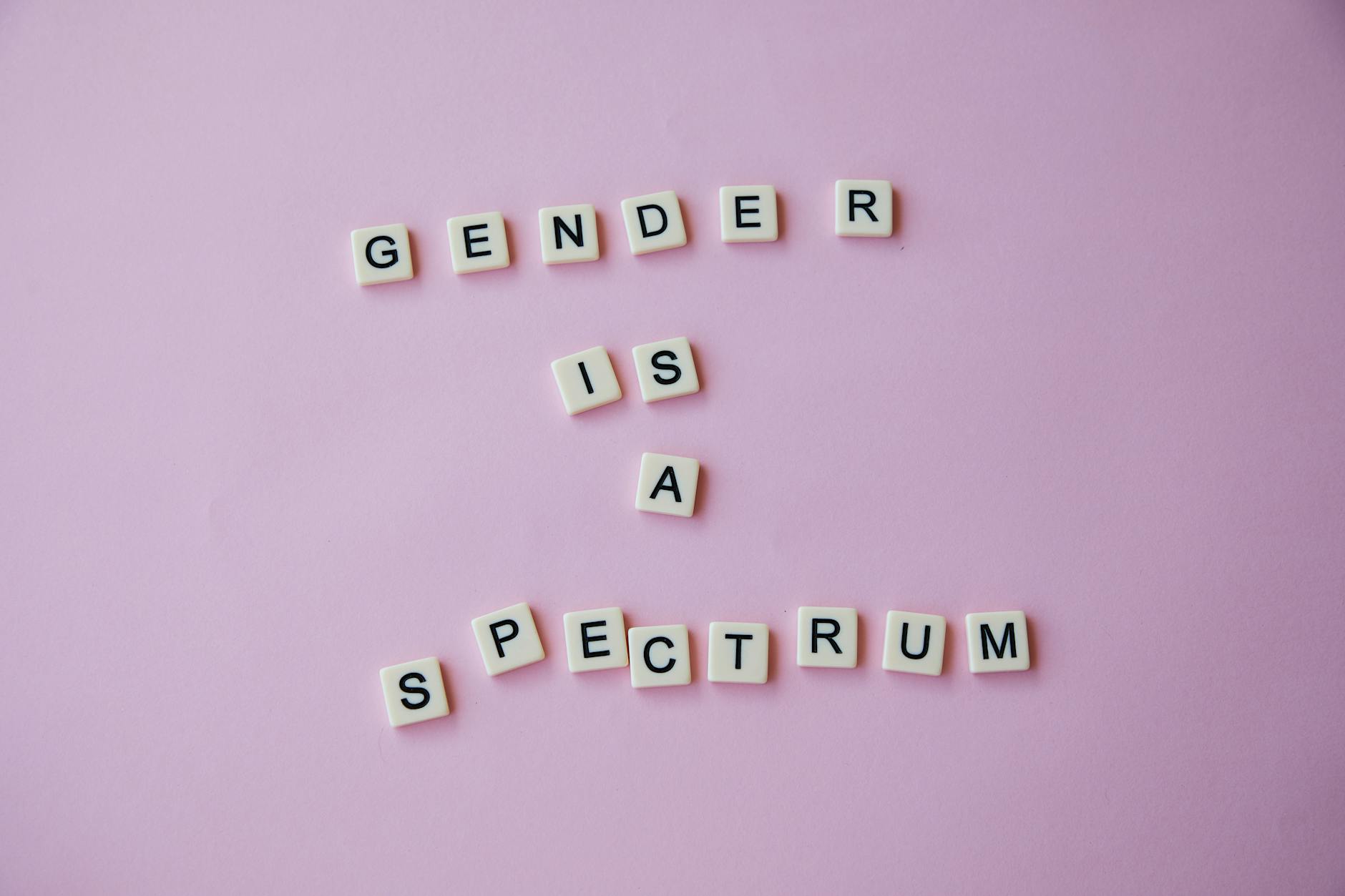 inscription gender is a spectrum made of scrabble letters against pink background